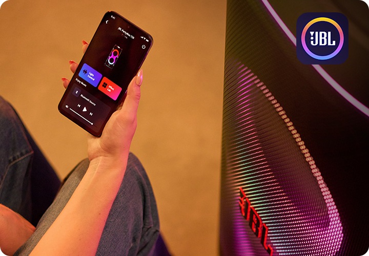 JBL PartyBox 앱을 켠 휴대폰을 든 사람 오른쪽 옆에는 스피커가 놓여 있습니다.