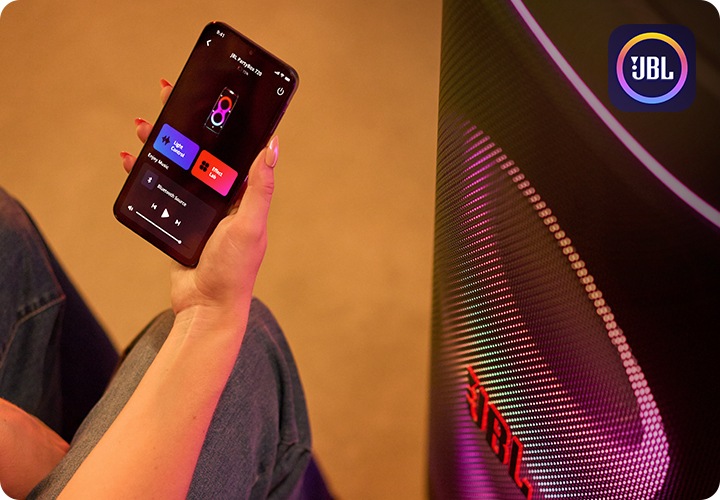 JBL PartyBox 앱을 켠 휴대폰을 든 사람 오른쪽 옆에는 스피커가 놓여 있습니다.