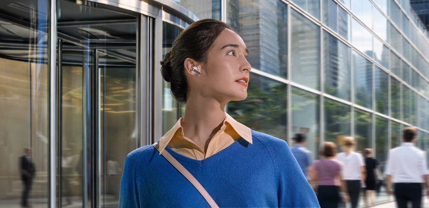 빌딩 앞에 한쪽 귀에 화이트 색상의 갤럭시 버즈4 이어버드를 착용한 여성이 오른쪽으로 고개를 향하고 있습니다.