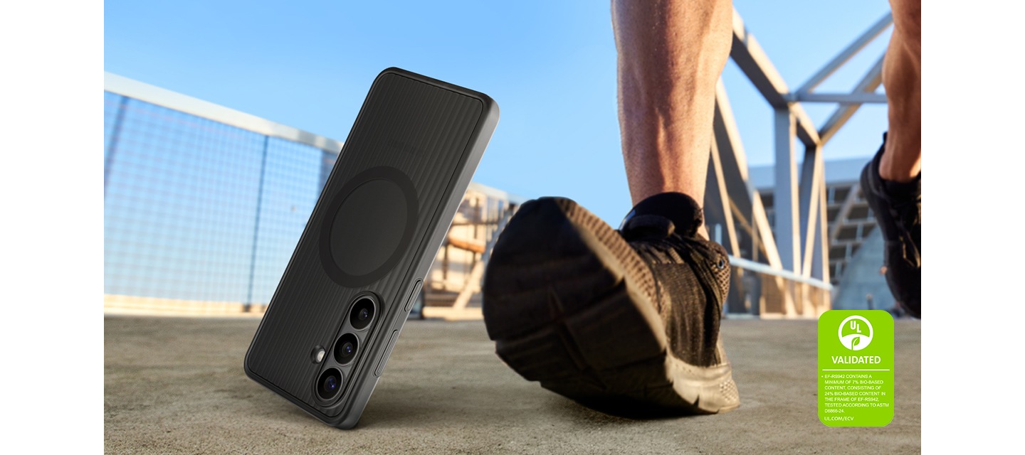 블랙 색상의 러기드 마그넷 케이스를 장착한 갤럭시 S26이 한 사람의 발걸음 옆의 지면 위로 떨어지고 있습니다. 이를 통해 케이스의 내구성과 야외 사용의 적합성을 강조하고 있습니다. '러기드 마그넷 케이스는 최소 7%의 바이오 기반 소재를 포함하고 있으며, 케이스의 프레임에는 24%의 바이오 기반 소재가 포함되어 있습니다. ASTM D6866-24에 따라 테스트되었습니다. UL.COM/ECV'라는 내용이 UL 인증 마크와 함께 표시되어 있습니다.