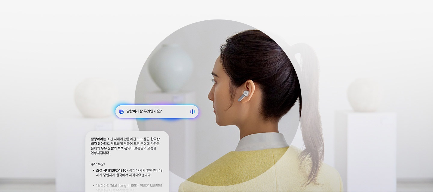 한쪽 귀에 화이트 색상 갤럭시 버즈4 프로를 착용한 여성의 뒷모습이 있습니다. 옆에는 AI에게 달항아리란 무엇인가요?라고 묻는 말풍선이 있습니다. 말풍선 아래에는 달항아리는 달항아리는 조선 시대에 만들어진 크고 둥근 한국산 백자 항아리로 부드럽게 부풀어 오른 구형에 가까운 몸체와 우유 빛깔의 백색 유약이 보름달의 모습을 연상시킵니다. 라는 답변이 담긴 다른 말풍선이 있습니다. 그 아래에는 달항아리의 주요 특징들이 나열되어 있습니다.