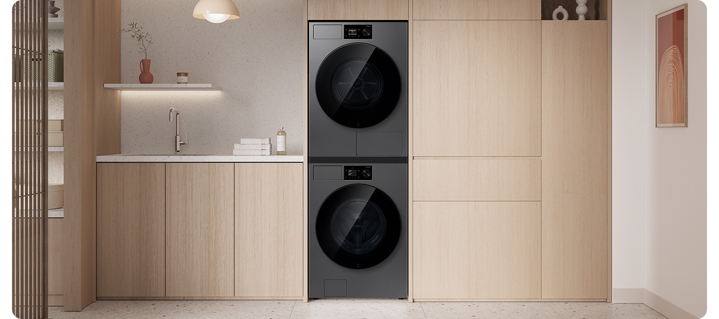 밝은 우드톤 붙박이장에 건조기&세탁기 패키지가 직렬로 설치되어 있습니다. 좌측 하부장 위에는 수건 등의 오브제가 놓여있는 연출된 이미지입니다.