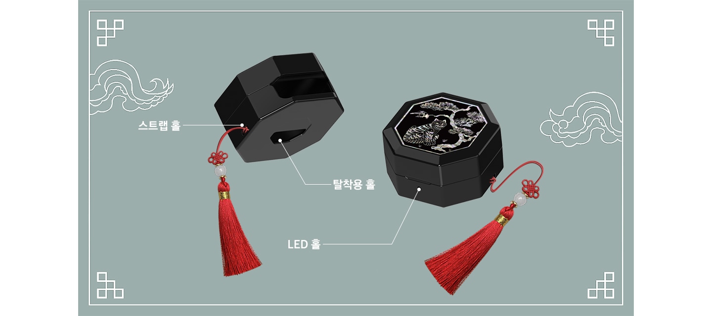 푸른색 배경에 전통 문양 이 그려져 있고, 갤럭시 버즈4｜버즈4 프로 케이스 (호랑이 전통 문양) 두 개가 있습니다. 좌측 제품은 뒤쪽의 좌측 하단을 향하고 있고 우측의 스트랩 홀과 하단의 탈착용 홀이 드러나 있으며 각각에 맞는 텍스트와 선이 이어져 있습니다. 우측의 제품은 앞면의 LED 홀이 드러나 있고 해당 텍스트와 선이 이어져 있습니다.