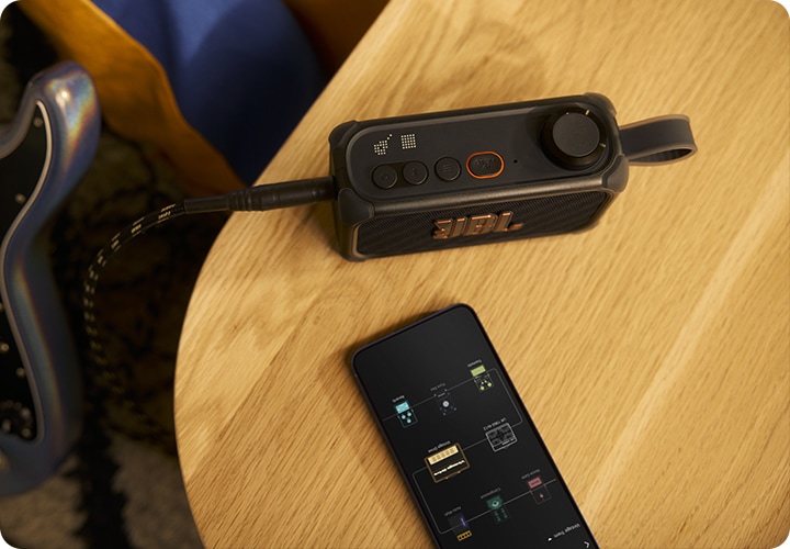 테이블 위에 BANDBOX SOLO와 휴대폰이 놓여 있습니다. 휴대폰 화면에는 BANDBOX SOLO와 연결된 앱 화면이 켜져 있습니다.