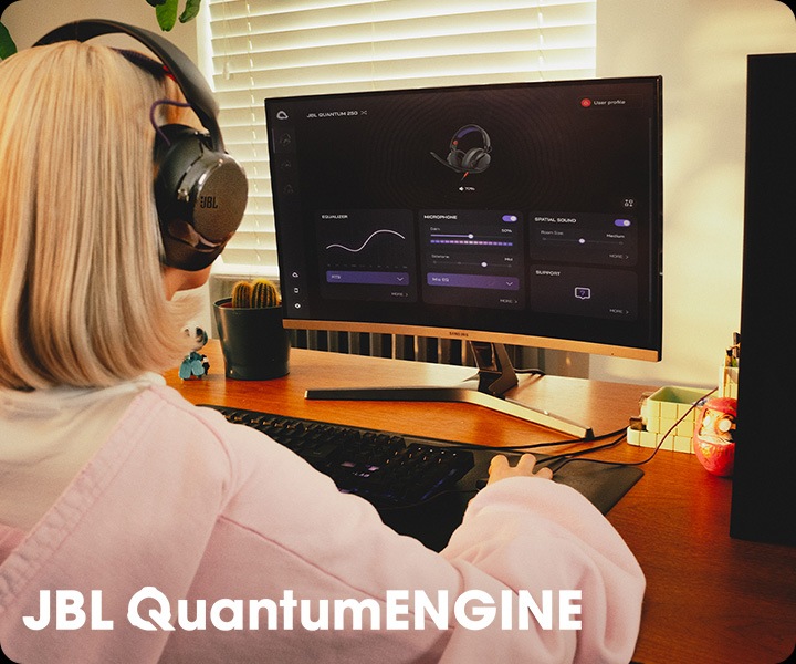 블랙 색상의 헤드폰을 착용한 여성이 컴퓨터로 JBL QuantumENGINE 대시보드를 보고 있습니다.
