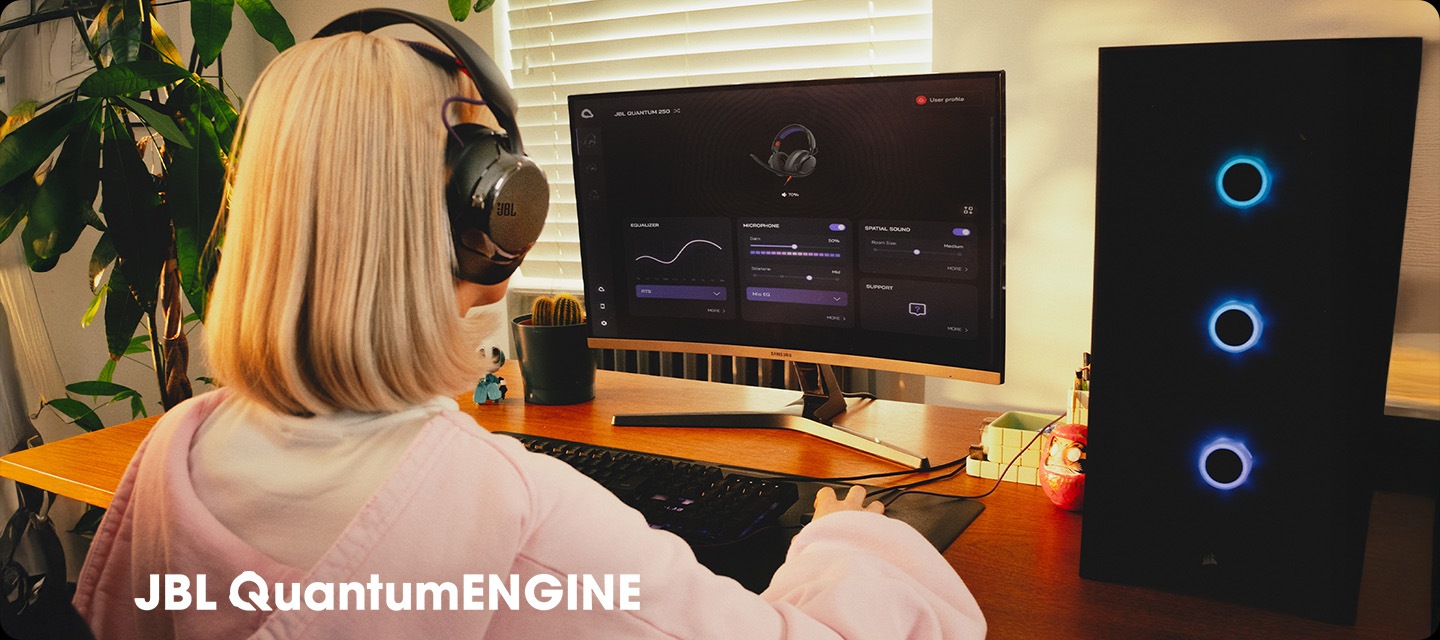 블랙 색상의 헤드폰을 착용한 여성이 컴퓨터로 JBL QuantumENGINE 대시보드를 보고 있습니다.