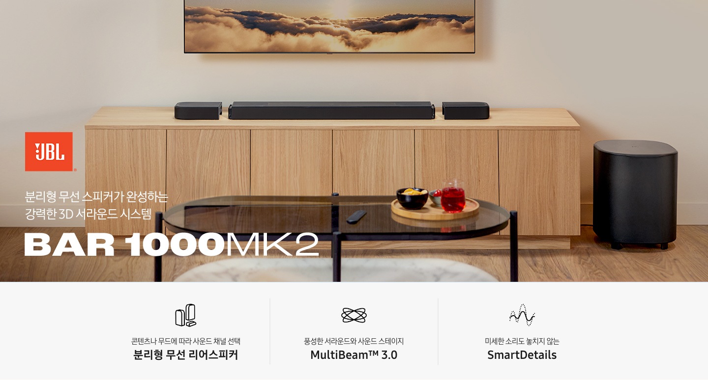 장식장 위에 사운드바가 놓여 있으며, 장식장 오른쪽 옆에는 서브우퍼가 놓여 있습니다. 장식장 앞에는 유리로 된 테이블이 놓여 있으며, 테이블 위에는 리모컨과 쟁반이 놓여 있고, 쟁반 위에는 다과가 놓여 있습니다. 왼쪽 하단에는 JBL 로고와 ‘분리형 무선 스피커가 완성하는 강력한 3D 서라운드 시스템‘ 문구와 스피커의 모델명인 ‘BAR 1000MK2’가 기재되어 있습니다. 이미지 하단에는 ‘콘텐츠나 무드에 따라 사운드 채널 선택 분리형 무선 리어스피커‘, ‘풍성한 서라운드와 사운드 스테이지 MultiBeam™ 3.0’, ‘미세한 소리도 놓치지 않는 SmartDetails’ 문구와 아이콘이 있습니다.