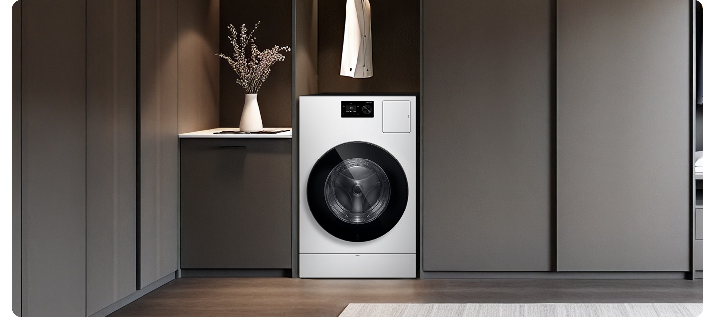 벽면 붙박이장에 AI 콤보가 설치되어 있고 위에 흰색 셔츠가 걸려있습니다. 좌측에는 어두운 그레이톤 하부장 위에 화분이 올려져있고 우측으로는 동일한 톤의 붙박이장이 나와있는 연출된 인테리어 이미지 입니다.