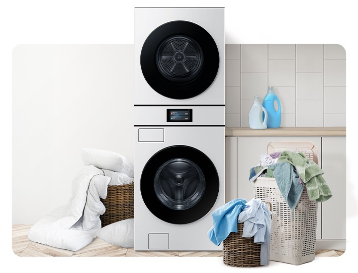 Bespoke AI 원바디가 중앙에 나와있고 좌측 뒷편 라탄 바구니에 의류가 가득 쌓여있고 앞쪽에 이불이 나와있습니다. 우측 파란색 플라스틱 바구니에도 수건 등 각종 옷감이 가득 쌓여있는 연출된 이미지입니다.