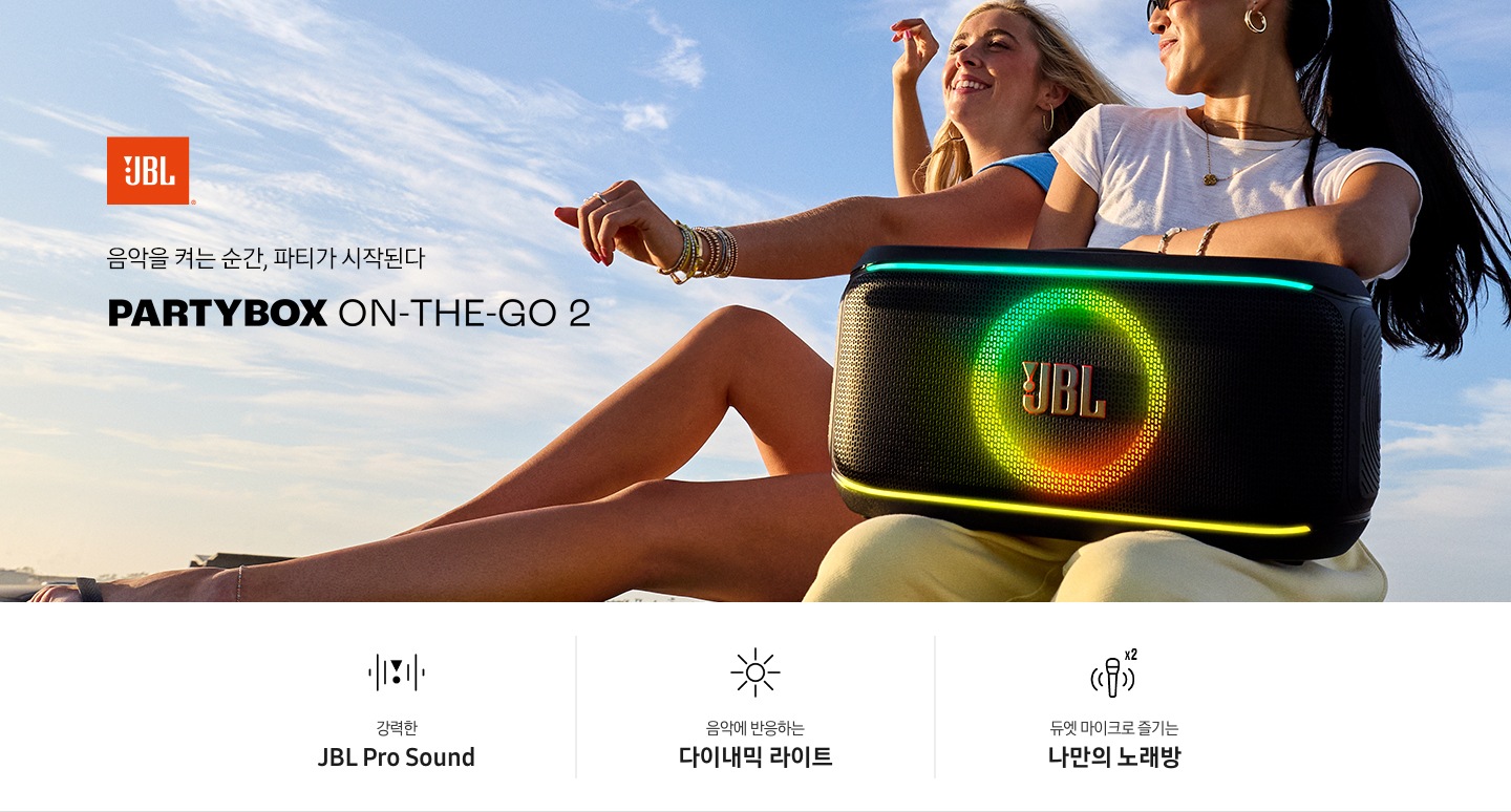 여성 두명이 앉아 있습니다. 흰색 티를 입은 여성이 스피커를 무릎에 올려 두었습니다. 왼쪽에는 JBL 로고와 ‘음악을 켜는 순간, 파티가 시작된다‘ 문구와 모델명인 ‘PARTYBOX ON-THE-GO 2’가 기재되어 있습니다. 이미지 하단에는 ‘강력한 JBL Pro Sound’, ‘음악에 반응하는 다이내믹 라이트‘, ‘듀엣 마이크로 즐기는 나만의 노래방‘ 문구와 아이콘이 있습니다.