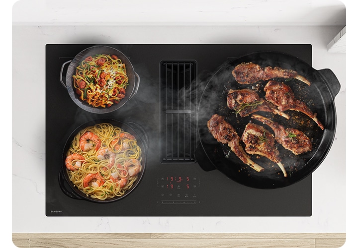 흰색 대리석 상판과 설치된 Infinite Line 후드일체형 인덕션을 위에서 내려보는 각도의 이미지가 나타나 있고 이미지 인덕션 왼쪽 부분에는 요리가 완성된 스테이크의 모습이 노출되고 있습니다. 인덕션 위에는 각각 파스타 2종류와 고기를 요리하고 있는 냄비와 팬의 모습과 발생하는 연기가 인덕션 중간에 내장된 후드로 빨려 들어가는 모습이 있습니다.