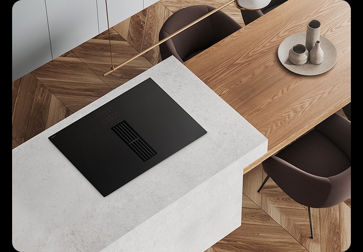 헤링본 마루가 깔린 바닥과 화이트 톤의 주방을 위에서 내려본 각도를 배경으로 이미지 왼쪽 부분에는 화이트 색상의 상판과 설치된 Infinite Line 후드일체형 인덕션이 노출되고 있고 인덕션 오른쪽 부분에는 상판과 연결되어 있고 우드로 제작된 테이블이 있습니다. 테이블 주위에는 진한 브라운 색상에 1인용 의자 4개가 놓여있습니다.