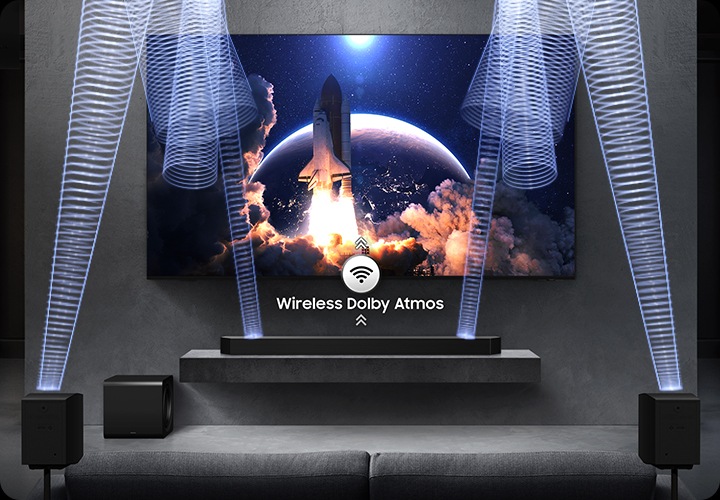 벽에 TV가 설치되어 있으며, 하단 장식장에는 사운드바가 설치되어 있습니다. 장식장 왼쪽 아래에는 서브우퍼가 놓여 있고, 소파 양 옆에는 무선 리어 스피커가 설치되어 있습니다. 사운드바와 무선 리어 스피커에서 음향효과가 나오고 있습니다.