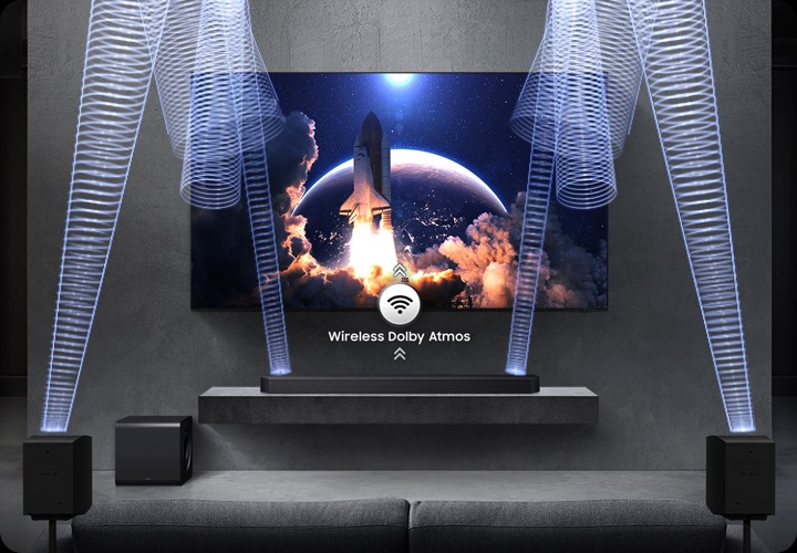 벽에 TV가 설치되어 있으며, 하단 장식장에는 사운드바가 설치되어 있습니다. 장식장 왼쪽 아래에는 서브우퍼가 놓여 있고, 소파 양 옆에는 무선 리어 스피커가 설치되어 있습니다. 사운드바와 무선 리어 스피커에서 음향효과가 나오고 있습니다.