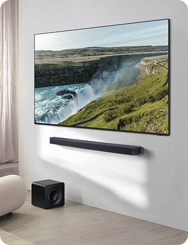 거실 벽에 TV와 사운드바가 설치되어 있으며, 사운드바 아래에는 서브우퍼가 놓여 있습니다.