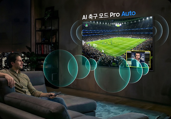 남성이 소파에 앉아서 벽에 설치된 TV를 보고 있습니다. TV 화면에는 축구 경기가 보여지고 있습니다.