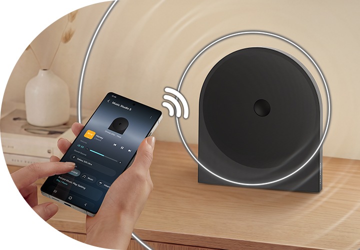 장식장 위에 스피커가 놓여 있습니다. 스피커와 연결된 휴대폰이 스피커의 설정을 조정하고 있습니다