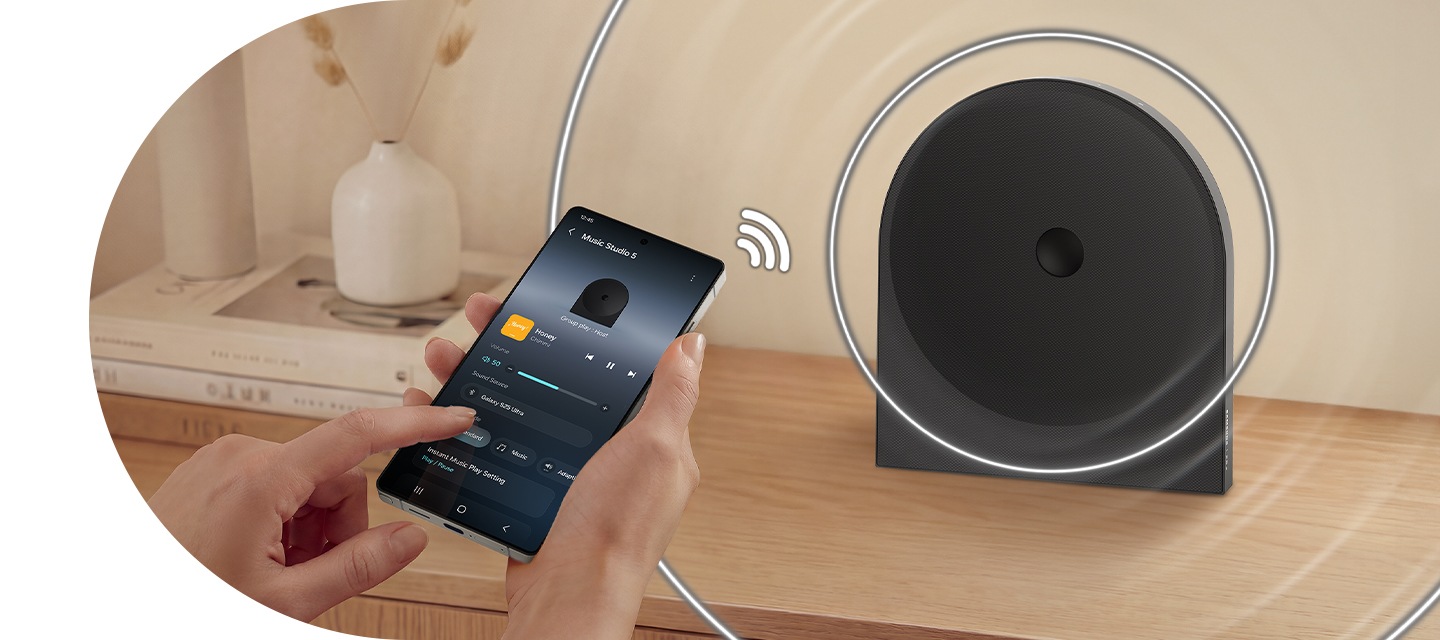 장식장 위에 스피커가 놓여 있습니다. 스피커와 연결된 휴대폰이 스피커의 설정을 조정하고 있습니다