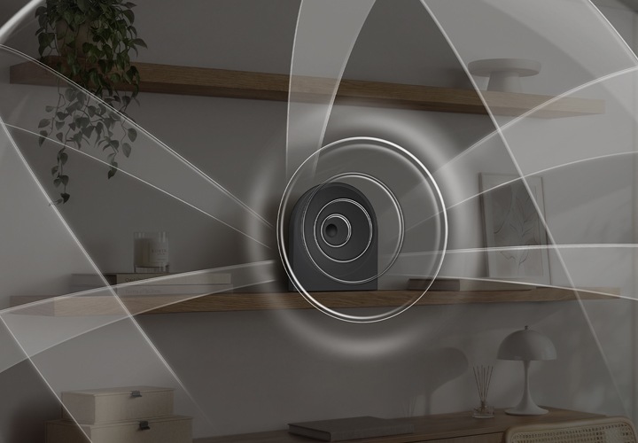 선반 위에 음향효과가 퍼져 나오는 스피커가 놓여 있습니다. 스피커 왼쪽에는 책들과 향초가 놓여 있으며, 오른쪽에는 책과 액자가 놓여 있습니다. 스피커 위쪽 선반에는 화분이 아래쪽 선반에는 조명, 방향제, 책, 서랍 등이 놓여 있습니다. 