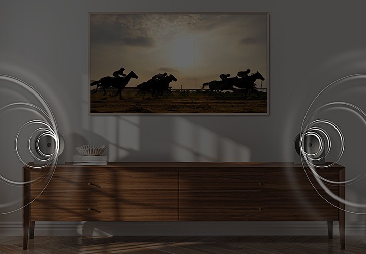 벽에 TV가 설치되어 있으며, 화면에는 말을 탄 사람들이 경주를 하고 있습니다. TV 아래는 장식장이 놓여 있으며, 장식장 양 끝에는 음향효과가 나오고 있는 스피커가 각각 놓여 있습니다.