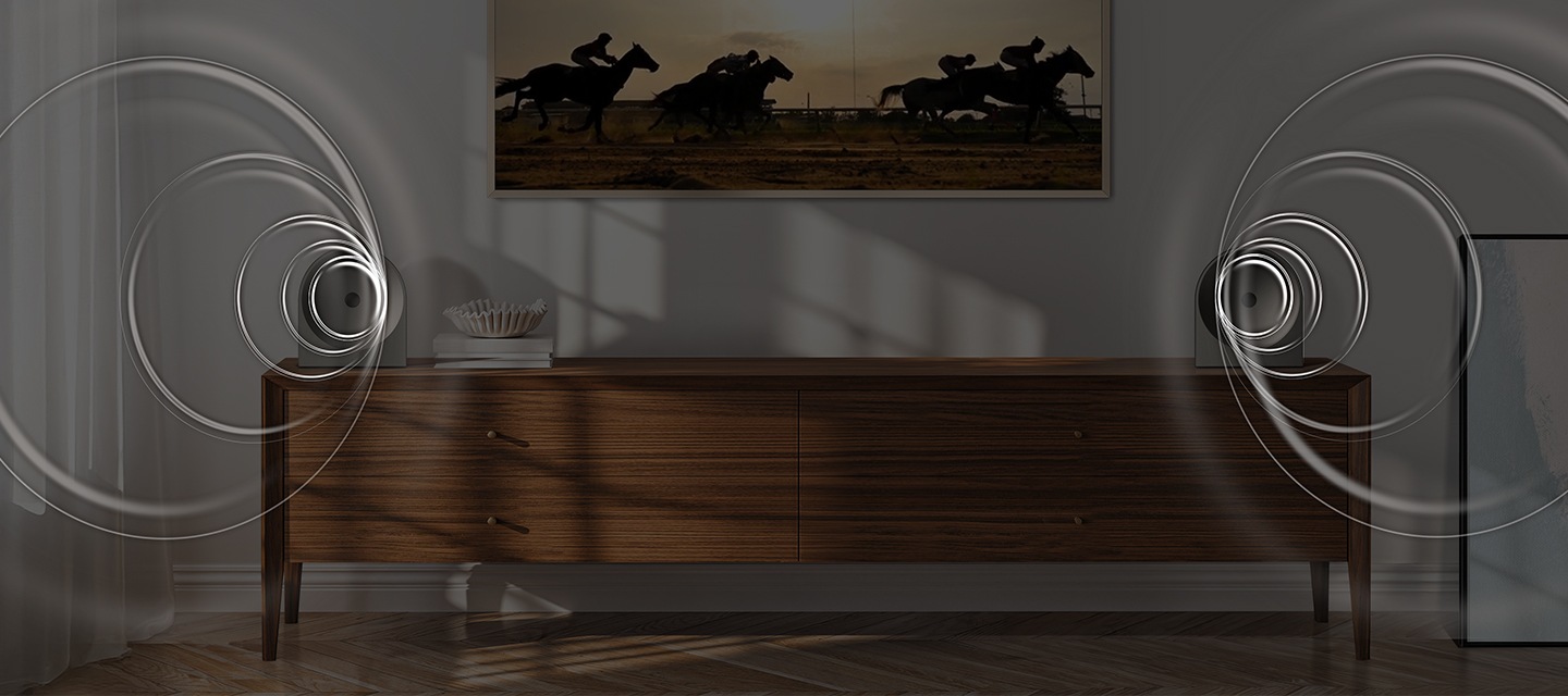 벽에 TV가 설치되어 있으며, 화면에는 말을 탄 사람들이 경주를 하고 있습니다. TV 아래는 장식장이 놓여 있으며, 장식장 양 끝에는 음향효과가 나오고 있는 스피커가 각각 놓여 있습니다.