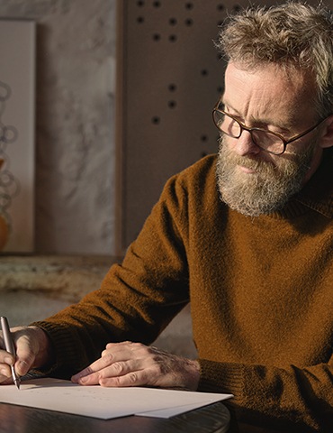 디자이너 에르완 부훌렉이 앉아서 종이 위에 글을 쓰고 있습니다.