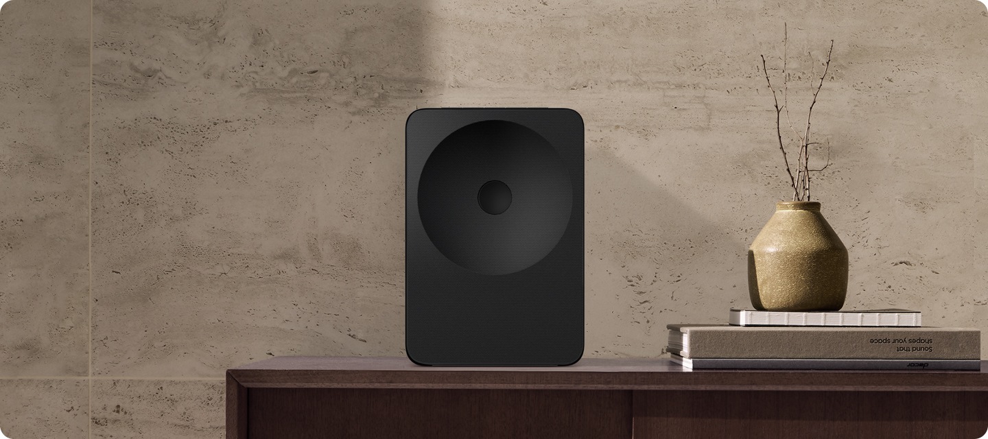 장식장 위에 스피커가 놓여 있습니다. 스피커 오른쪽에는 책들과 화병이 놓여 있습니다.