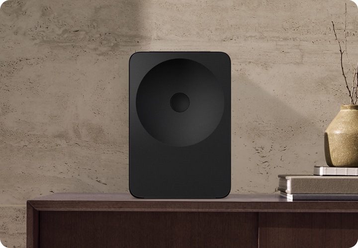 장식장 위에 스피커가 놓여 있습니다. 스피커 오른쪽에는 책들과 화병이 놓여 있습니다.