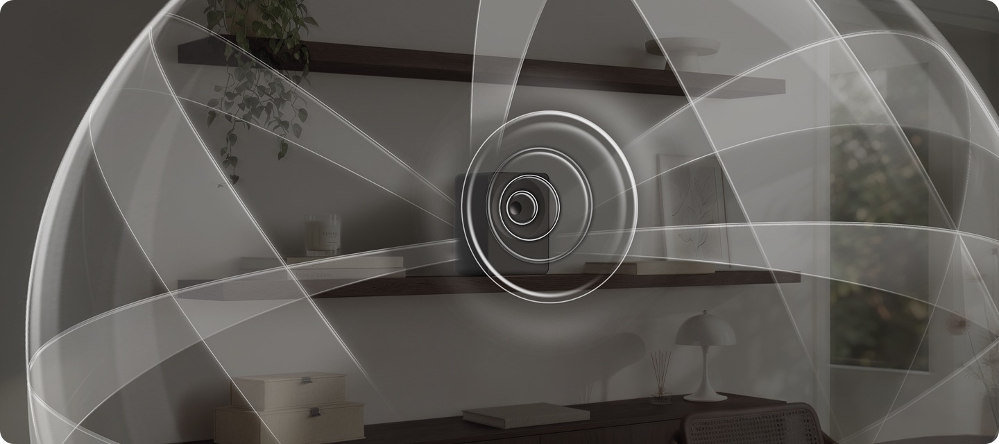 선반 위에 음향효과가 퍼져 나오는 스피커가 놓여 있습니다. 스피커 왼쪽에는 책들과 향초가 놓여 있으며, 오른쪽에는 책과 액자가 놓여 있습니다. 스피커 위쪽 선반에는 화분이 아래쪽 선반에는 조명, 방향제, 책, 서랍 등이 놓여 있습니다. 