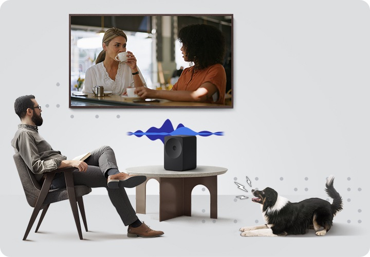 의자에 앉은 남성이 벽에 설치된 TV를 보고 있으며, 화면에는 영화의 한 장면이 나옵니다. 남성 앞에는 테이블이 놓여 있으며, 테이블 위에는 스피커가 놓여 있습니다. 스피커 위에는 음향효과가 나오고 있습니다. 테이블 오른쪽에는 강아지가 엎드려서 짖고 있습니다.