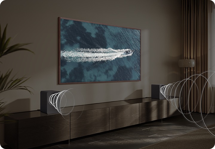 벽에 TV가 설치되어 있으며, 화면에는 바다 위에 요트가 지나가고 있습니다. TV 아래는 장식장이 놓여 있으며, 장식장 양 끝에는 음향효과가 나오고 있는 스피커가 각각 놓여 있습니다.