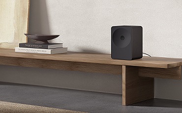 선반 위에 스피커가 놓여 있습니다. 스피커 왼쪽에는 책 위에 접시가 올려져 있습니다.