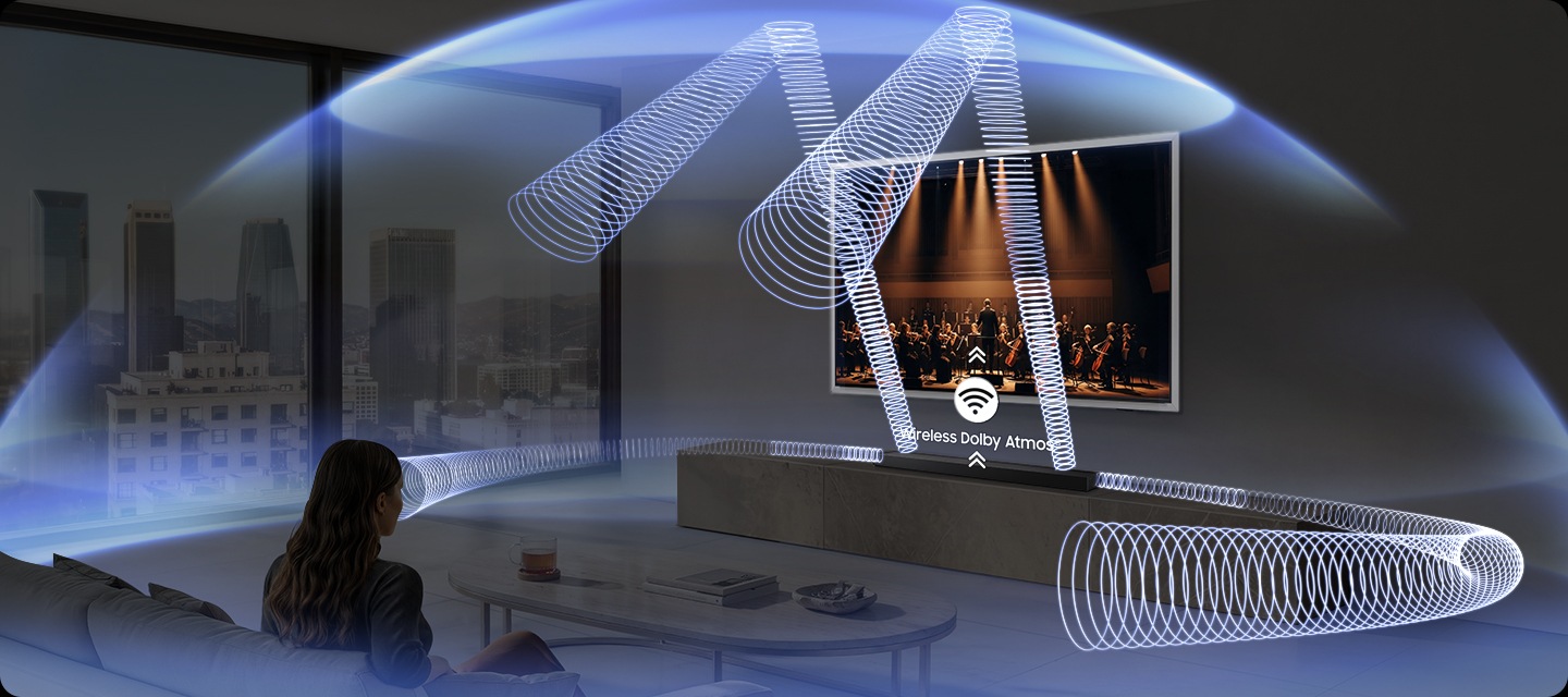 거실에 여성이 소파에 앉아서 벽에 설치된 TV를 보고 있습니다. TV 하단에는 사운드바가 설치된 장식장이 있습니다. 사운드바에서 음향효과가 나와 거실을 감싸고 있습니다.