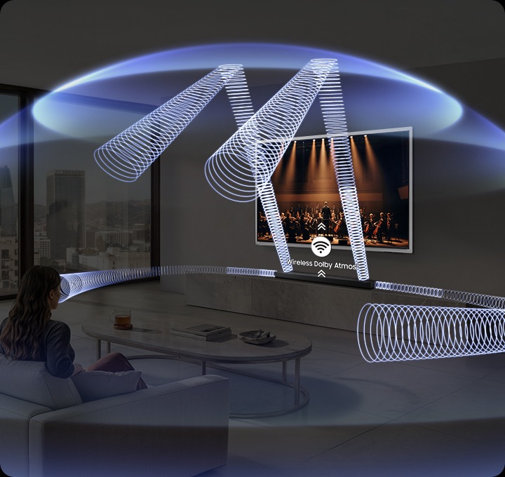 거실에 여성이 소파에 앉아서 벽에 설치된 TV를 보고 있습니다. TV 하단에는 사운드바가 설치된 장식장이 있습니다. 사운드바에서 음향효과가 나와 거실을 감싸고 있습니다.