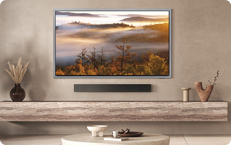 벽에 TV와 사운드바가 설치되어 있습니다. 사운드바 아래에는 장식장이 있으며, 장식장 위에는 화병과 장식품들이 놓여 있습니다.