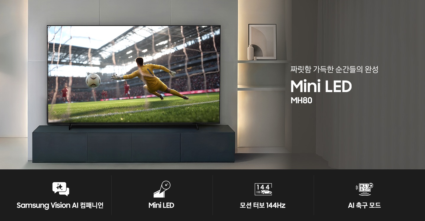 장식장 위에 TV가 설치되어 있습니다. TV 화면에는 축구 경기가 보여지고 있습니다. TV 오른쪽으로는 ‘짜릿함 가득한 순간들의 완성‘ 문구와 시리즈명인 ‘Mini LED’ 그리고 모델명인 ‘MH80’가 기재되어 있습니다. 이미지 하단에는 ‘Samsung Vision AI 캠패니언’, ‘Mini LED’, ‘모션 터보 144Hz‘, ‘AI 축구 모드‘ 문구 및 아이콘이 있습니다.