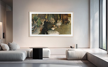 벽에 TV가 설치되어 있으며, 화면에는 명화가 보입니다. TV 앞에는 테이블과 소파들이 놓여 있습니다.