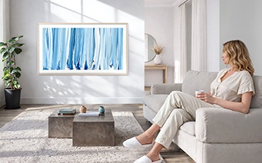 여성이 소파에 앉아 벽에 설치된 TV를 보고 있습니다.