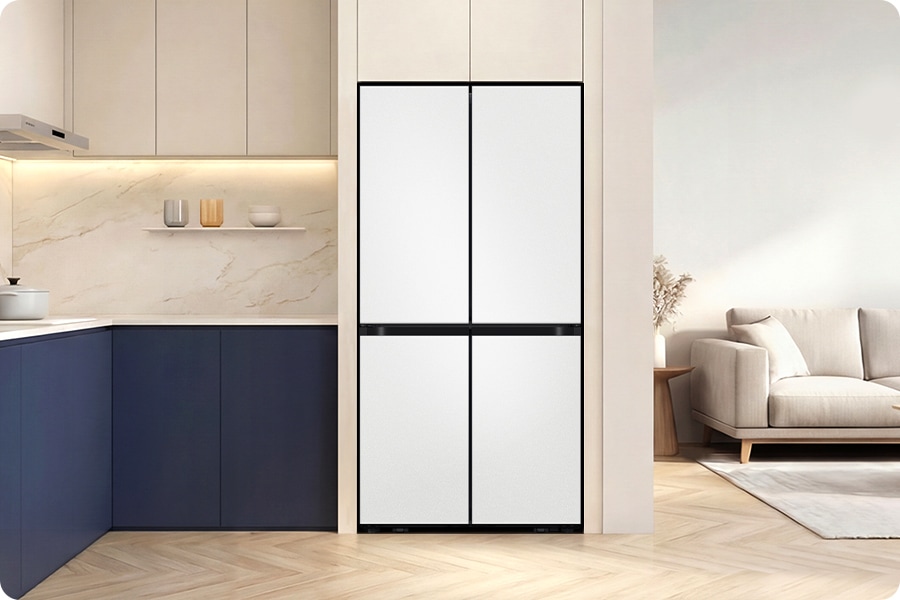1인 가구. 베이지톤 냉장고장에 냉장고 4도어가 설치되어 있습니다. 냉장고장 우측으로는 베이지색 쇼파와 러그가 있는 거실이 있고 좌측으로는 베이지색 상부장과 네이비색 하부장이 있으며, 위에 냄비와 선반 위 오브제가 놓여있는 연출된 이미지 입니다.