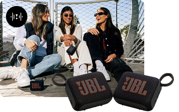 여성 3명이 바닥에 앉아 있습니다. 가운데 앉은 여성 손에 스피커 한 대, 왼쪽에 앉은 여성 발 쪽에 스피커 한 대가 있습니다. 확대된 스피커 두 대가 이미지 오른쪽 하단에 놓여 있습니다.