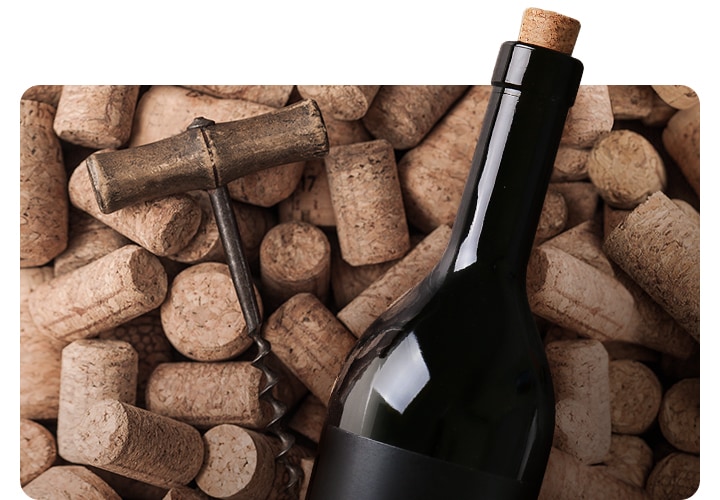 코르크 마개가 쌓여있고 그 위에 와인오프너와 와인병이 놓여있는 연출된 이미지 입니다.