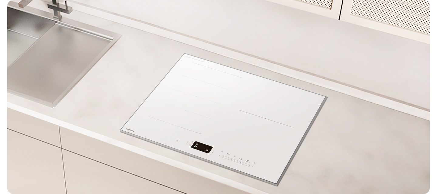 화이트 톤의 밝은 주방에 설치된 인덕션으로 확대한 이미지를 배경으로 이미지 중간 부분에는 아주 약간 회색빛이 도는 상판이 보이고 인덕션이 설치되어 있습니다. 인덕션 왼쪽 부분에는 싱크대의 오른쪽 부분이 약간 노출되어 있습니다.