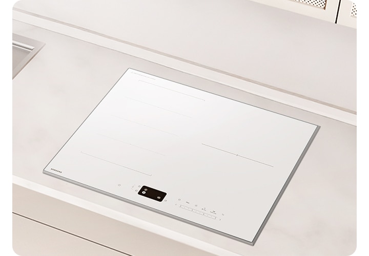 화이트 톤의 밝은 주방에 설치된 인덕션으로 확대한 이미지를 배경으로 이미지 중간 부분에는 아주 약간 회색빛이 도는 상판이 보이고 인덕션이 설치되어 있습니다. 인덕션 왼쪽 부분에는 싱크대의 오른쪽 부분이 약간 노출되어 있습니다.