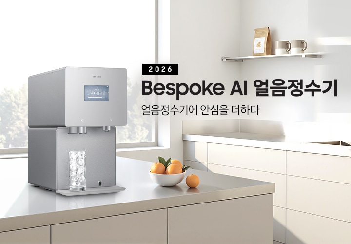 2026 Bespoke AI 얼음정수기. 얼음정수기에 안심을 더하다.  회색 테이블 위에 얼음정수기 사틴 그레이지 컬러가 설치되어 있는 측면 이미지 입니다. 정수기 얼음 토출구 아래에는 얼음이 가득 든 물컵이 놓여있습니다. 정수기 우측에는 오렌지가 가득 담긴 그릇이 놓여있습니다.