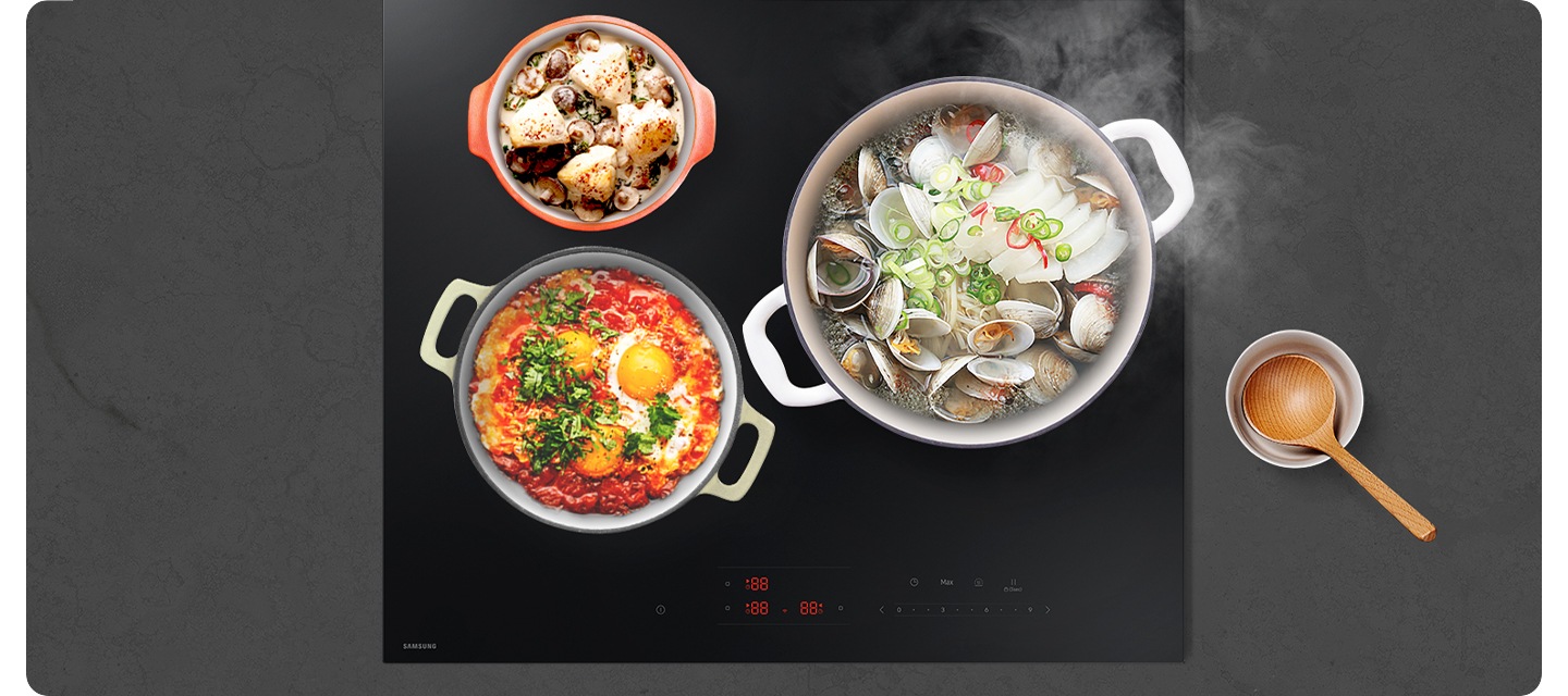 진한 회색 상판의 대리석을 배경으로 이미지 중간 부분에는 인덕션이 설치되어 있고 인덕션 위에는 각각 크기가 다른 냄비 3개에서 음식을 조리 중인 모습이 있습니다. 인덕션 오른쪽 부분에는 그릇 안에 나무 국자가 놓여 있습니다.