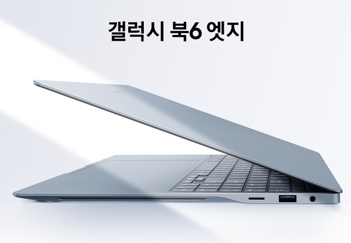 그레이블루 색상의 갤럭시 북6 엣지가 살짝 열린 상태로 왼쪽을 향해 측면 모습을 드러내고 있습니다. 키보드와 터치패드 일부도 드러나 있습니다. 왼쪽에서 비스듬한 빛줄기가 장면을 가로지르고 있습니다.