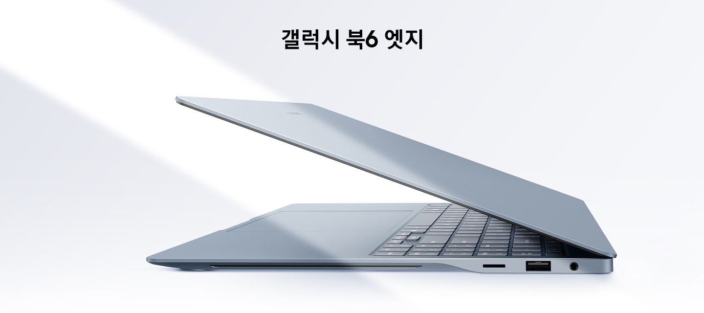그레이블루 색상의 갤럭시 북6 엣지가 살짝 열린 상태로 왼쪽을 향해 측면 모습을 드러내고 있습니다. 키보드와 터치패드 일부도 드러나 있습니다. 왼쪽에서 비스듬한 빛줄기가 장면을 가로지르고 있습니다.