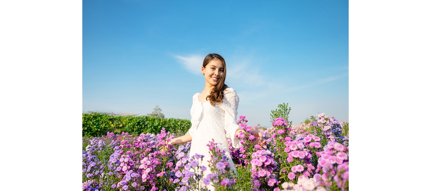 하얀 드레스를 입은 여성이 꽃밭 한가운데 서서 사진을 찍고 있는 모습입니다.