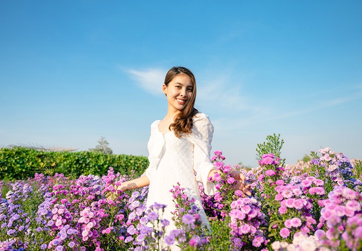 하얀 드레스를 입은 여성이 꽃밭 한가운데 서서 사진을 찍고 있는 모습입니다.