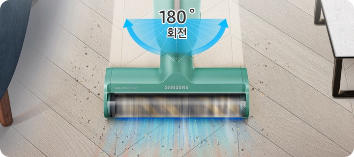 헤링본 마루가 깔린 거실 바닥을 배경으로 이미지 오른쪽 부분에는 화이트 상판의 테이블이 놓여 있고 이미지 왼쪽 부분에는 진한 남색 패브릭 소재의 소파 다리 부분이 노출되고 있습니다. 이미지 중간 부분에는 슬림 소프트마루 브러시로 청소를 하며 먼지를 흡입하는 모습의 이미지가 있고 슬림 소프트마루 브러시가 지나간 자리는 먼지가 있는 부분과는 달리 밝은 색으로 깨끗해진 모습을 알려주고 있습니다.